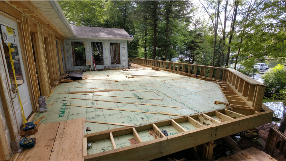 Large elevated deck under construction, featuring green subfloor panels and surrounding forested area.