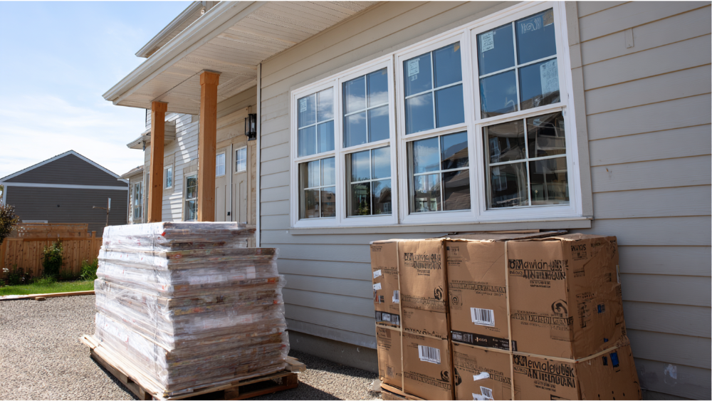 New vinyl windows stacked outside a home under construction, ready for installation.